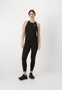 Débardeur actif noir et leggings ajustés en tissu extensible. Conception avec un logo en haut à gauche. Complété par des chaussures de sport noires.