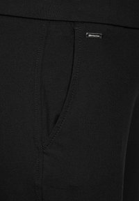 Pantalones de algodón negros con un bolsillo lateral, textura suave, cintura elástica y una pequeña etiqueta de marca cerca de la cintura.