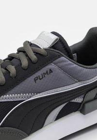 Zapatilla deportiva en negro y gris con materiales de malla y sintéticos. Cuenta con cordones, un collar acolchado, el logotipo de Puma y franjas laterales distintivas.