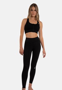 Zwarte sportoutfit met een crop top met een rits aan de voorkant en high-waisted leggings, beide gemaakt van een soepele, rekbare stof.