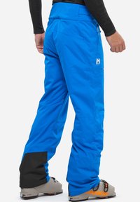 Blaue Skihosen aus wasserdichtem Material, mit einem schwarzen unteren Saum, mehreren Taschen und einem Logo an der Seite. Entworfen für Wintersportarten.