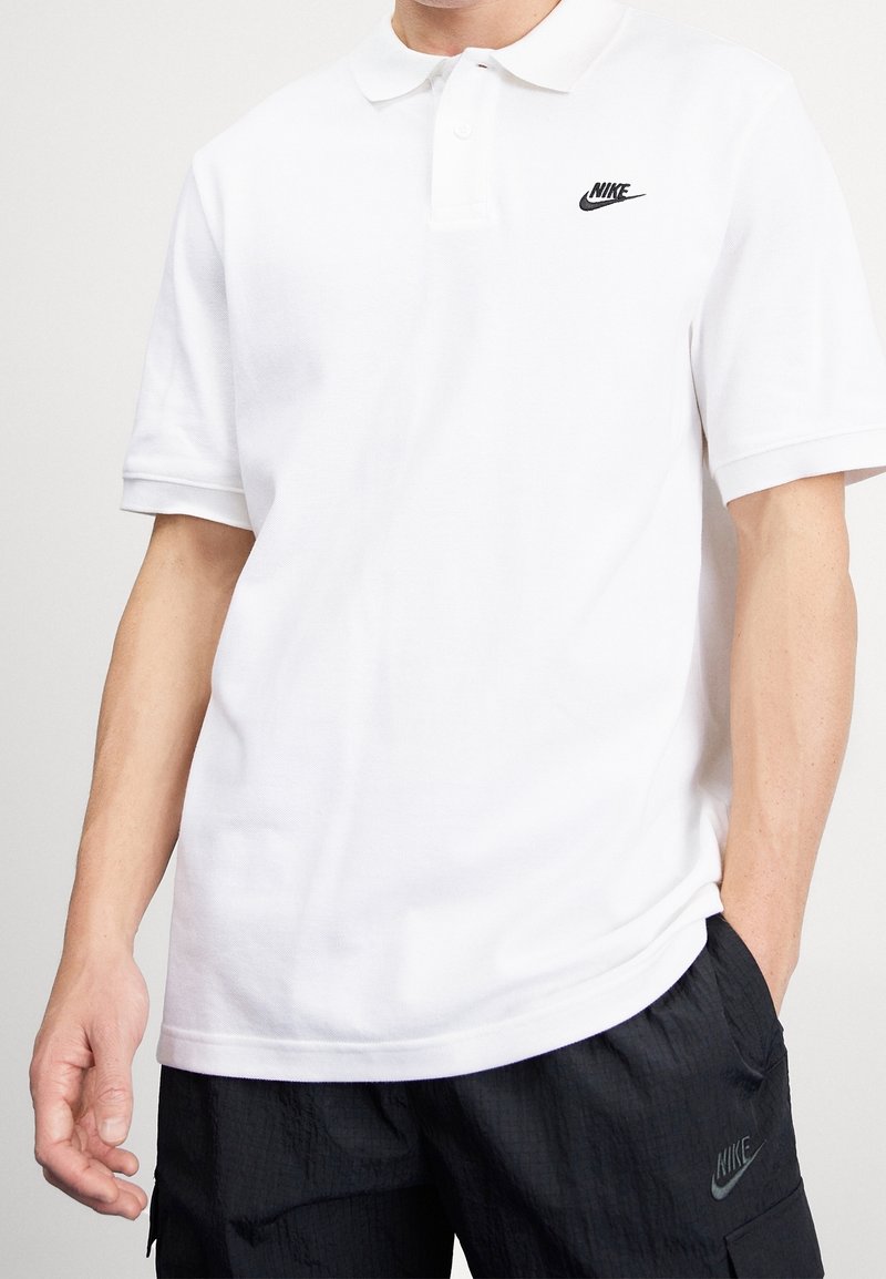 Polo blanc en coton, arborant un logo Nike noir sur la poitrine gauche. Manches courtes et col classique.