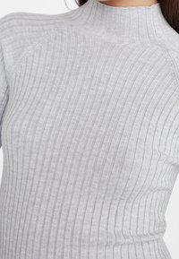 Jasnoszara bluzka z długim rękawem o pionowej prążkowanej fakturze, z wysokim kołnierzem i dopasowanym krojem, wykonana z miękkiego, elastycznego materiału.