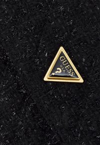 Triangular black and gold Guess U.S.A. logo on textured black fabric with shiny fibers.