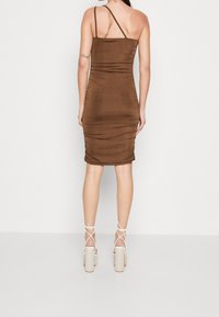 Hnědé upnuté šaty s řasenou texturou, jednoramenným designem a délkou po kolena. Kombinované s páskovými, světle zbarvenými platformovými podpatky.