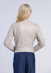 Ljusbeige läderjacka med en figurnära passform och ribbat nederkant. Har en liten logotyp på baksidan och långa ärmar.
