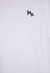 Weißes kurzärmliges T-Shirt aus Baumwolle, mit einer kleinen schwarzen gestickten "Mr." auf der linken Brust. Glatte Textur und lässiges Design.
