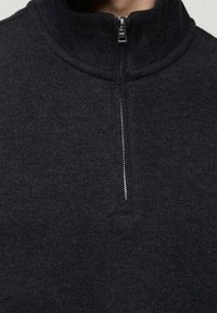 Zwarte quarter-zip pullover van textuurstof. Voorzien van een hoge kraag en een zilveren rits. Eenvoudig, minimalistisch ontwerp.