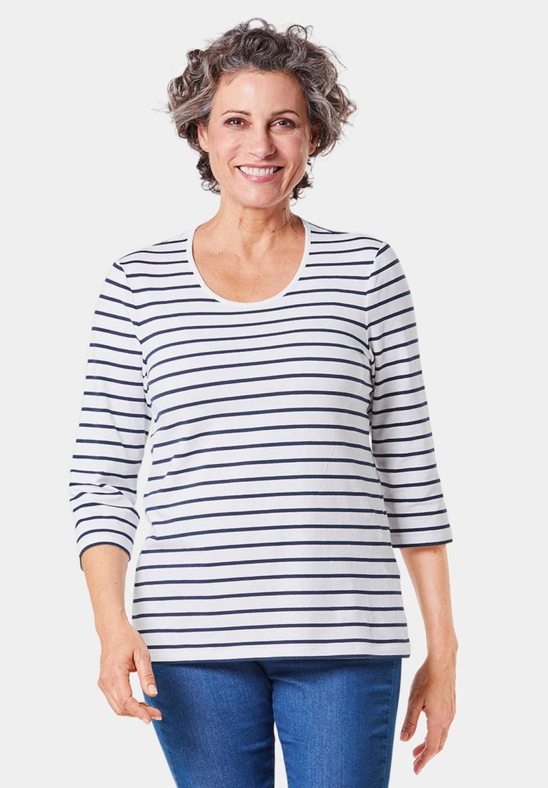 Witte blouse met lange mouwen en marineblauwe strepen, met een ronde hals en een zachte textuur, gecombineerd met blauwe spijkerbroek.