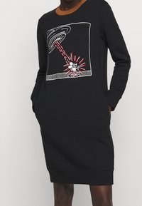 Svart sweatshirtklänning med långa ärmar, med en brun krage och ett grafiskt tryck av en UFO som strålar ner röda och vita strålar.