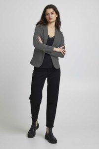 Blazer gris con un ajuste entallado, acompañado de una blusa de encaje negra, combinado con pantalones negros y botas negras de tobillo gruesas.