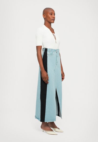 Gonna maxi in denim con tessuto blu chiaro e pannelli laterali neri, spacchi davanti e vita alta. Indossata con un top bianco a coste e tacchi crema.