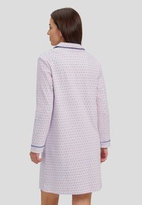 Camisa de noche de manga larga en algodón rosa claro con un patrón circular, con cuello en pico y ribete azul marino en los puños.