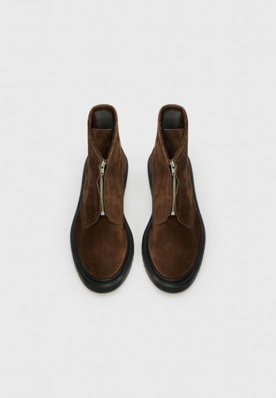Bottines en daim marron à zip sur le devant, avec une semelle épaisse en caoutchouc noir et une texture lisse. Aucun motif ni accent visible.