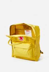 Gul tygryggsäck med ett dragkedjat huvudfack, framficka och logotypmärke. Slät textur med hållbart syntetmaterial.