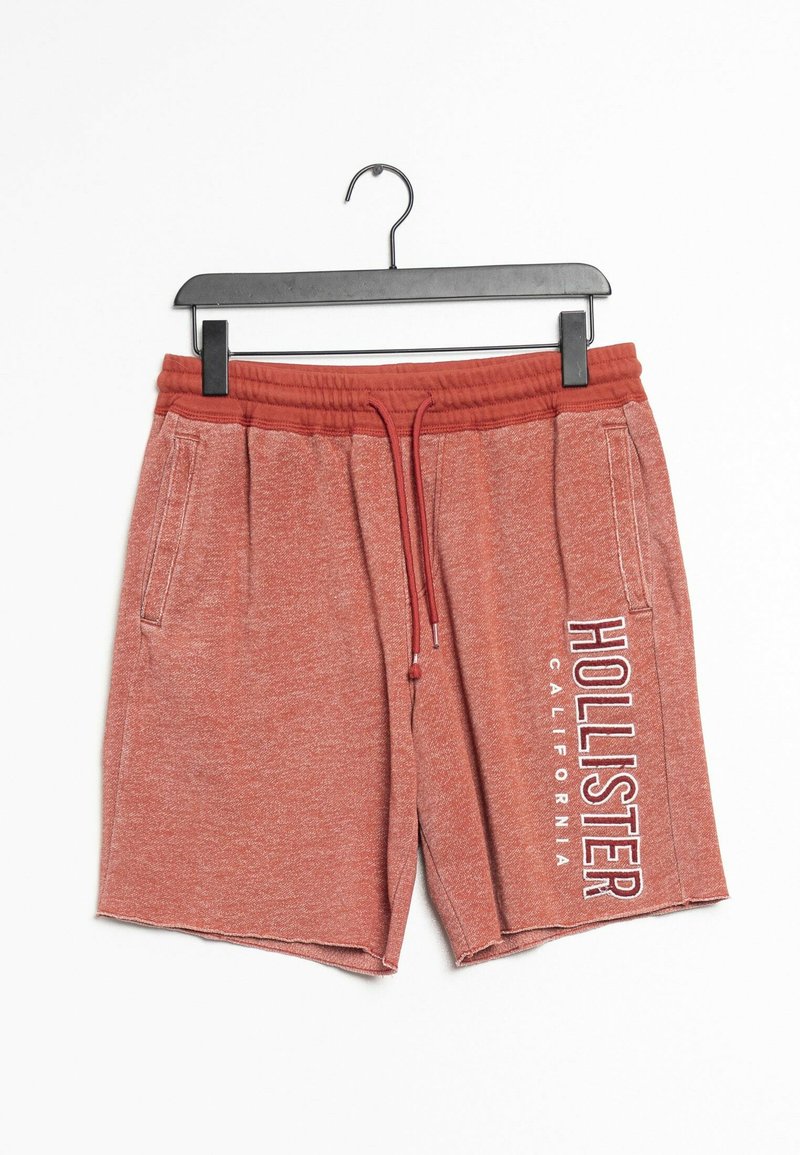 Shorts rouges chinés avec une taille élastique, un cordon de serrage et des poches latérales. Présente un logo en texte blanc sur la jambe gauche. Texture de tissu douce.