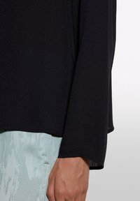 Svart långärmad topp med en slät textur och avslappnad passform, i kombination med ljusblå texturerade byxor, som visar kontrasterande färger.