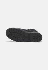 Black rubber boot sole with deep tread patterns, textured surface, and raised sections for grip. Logo embossed on the side.