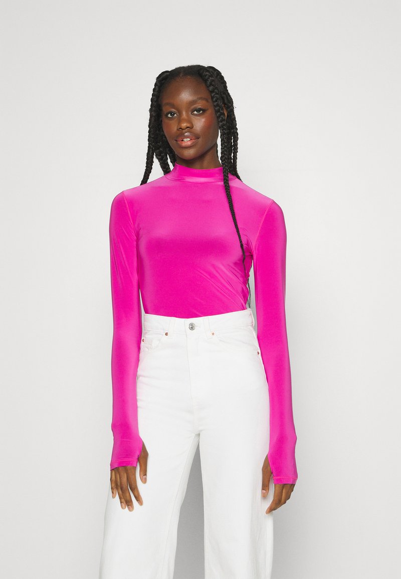 Haut à manches longues ajusté de couleur rose vif, fabriqué à partir d'un matériau lisse. Associé à un pantalon blanc taille haute. Design élégant à col montant.