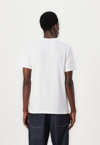 White cotton t-shirt with short sleeves, a crew neckline, and a relaxed fit, paired with dark blue denim jeans featuring contrasting stitching.
