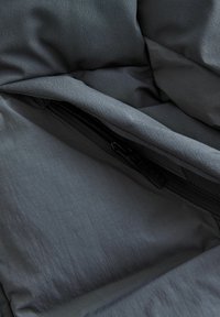 Intérieur en tissu rembourré gris montrant une texture lisse, avec une fermeture éclair noire et une étiquette de marque. Le design met l'accent sur la fonctionnalité et la chaleur.
