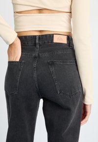 Čierne džínsy s vysokým pásom a miernym vyblednutím, so štvorcovou nášivkou značky a dvoma zadnými vreckami so šitím.