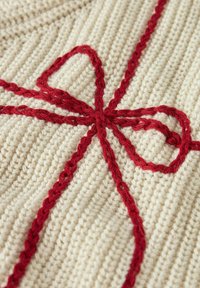 Tessuto lavorato a maglia di colore crema con un design intrecciato rosso. Il motivo forma una forma a fiocco, evidenziando un aspetto testurizzato e intrecciato.