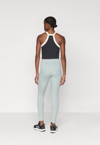 Črn športni crop top z belimi detajli, v kombinaciji s svetlim meteorsko zelenim visokim pasom legicami in črnimi športnimi čevlji. Gladka tkanina in prilega zasnova.