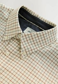 Button-up shirt in light cream fabric, featuring a grid pattern in brown and gray. Classic collar with cream buttons and dark interior lining.