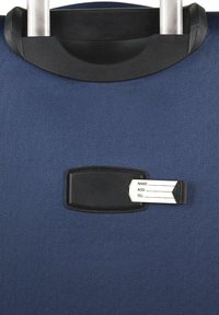 Maleta azul marino con un exterior texturizado, que incluye un soporte negro para etiqueta de identificación y una tarjeta blanca para detalles de contacto. Asa retráctil visible.