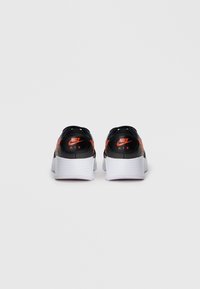 Melnas Nike kedas ar oranžiem akcentiem, kurām ir teksturēta virsma un balta gumijas zole. Veidotas ar zemu profilu un minimālistisku formu.