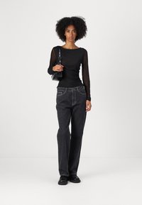 Black mesh long-sleeve top with fitted body and round neckline, paired with dark denim jeans featuring a relaxed fit and subtle texture.