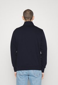 Felpa blu navy con colletto alto, polsini e orlo a coste. Realizzata in tessuto morbido con una superficie liscia, presenta un design semplice.