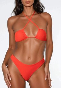 Set di bikini rosso composto da un top triangolare con spalline incrociate e un slip a vita bassa, entrambi realizzati in tessuto liscio e con copertura minima.
