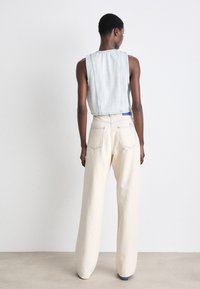 Lys blå cropped denimvest paret med løstsittende kremhvite vide bukser. Har kontrastsøm og baklommer.