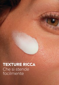 Crema ricca applicata sulla pelle, di colore bianco, mostrata in un primo piano di pelle textured, evidenziando la levigatezza e le proprietà di assorbimento.