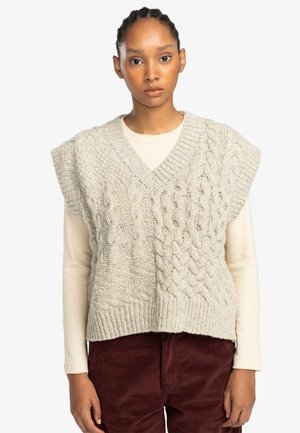 Cable-knit sweater vest in light gray. Features a v-neck, short sleeves, and textured patterns. Worn over a cream long-sleeve top.