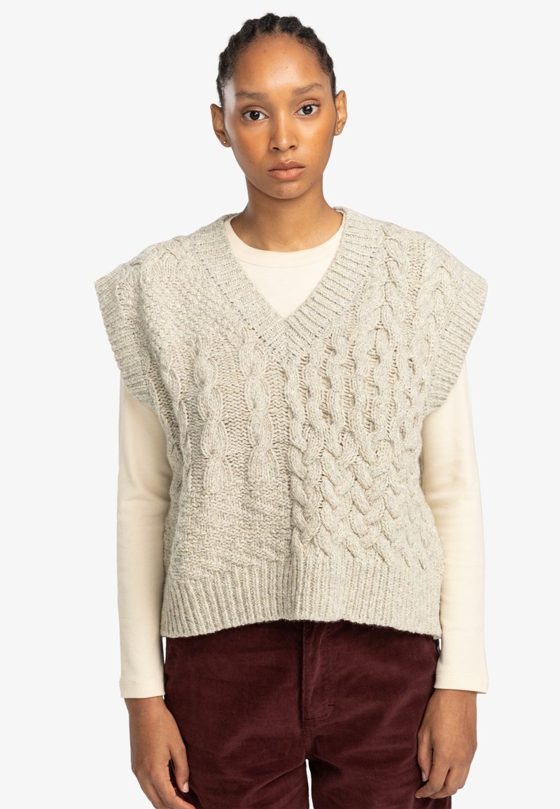 Cable-knit sweater vest in light gray. Features a v-neck, short sleeves, and textured patterns. Worn over a cream long-sleeve top.