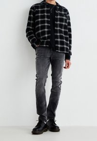 Camicia a quadri in bianco e nero di flanella sopra una maglia nera, abbinata a jeans grigi slim-fit e scarpe nere stringate. Tessuto morbido e vestibilità su misura.