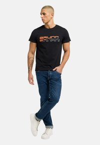 Sort bomulds T-shirt med et flerfarvet grafisk print på fronten. Matchet med mørkeblå jeans og hvide sneakers.