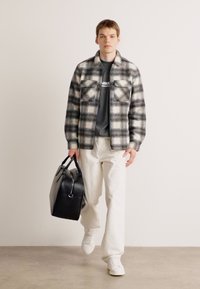 Plaid shirt in black and white, gray t-shirt, white pants, white sneakers, carrying a black leather bag with dual handles.