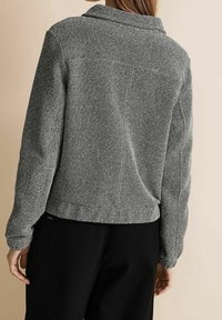 Szary wzorzysty żakiet z kołnierzykiem, długimi rękawami i luźnym krojem. Posiada teksturowaną tkaninę oraz elastyczny dół.