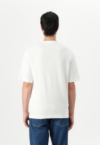 T-shirt en coton blanc à manches courtes, col rond, et un dos uni. Le tissu a une texture douce. Associé à un jean en denim bleu.
