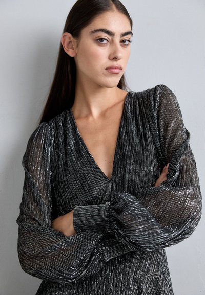 Robe noire avec texture en relief scintillante, décolleté en V profond et manches bouffantes transparentes. Présente un corsage ajusté et des détails froncés sur les manches.