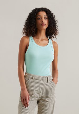 Hellblaues, geripptes Tanktop mit rundem Ausschnitt, kombiniert mit hochtaillierten Hosen in Weiß und Schwarz mit Streifen. Glatte Textur und figurbetontes Design.
