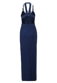 Granatowa sukienka wieczorowa z dopasowaną spódnicą, przezroczystymi koronkowymi plecami i teksturowanymi kwiatowymi ramiączkami. Posiada długą, smukłą sylwetkę.
