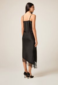 Svart sidenklänning med spetskant vid fållen. Har tunna justerbara band och en luftig design. Bärs med svarta klackskor.