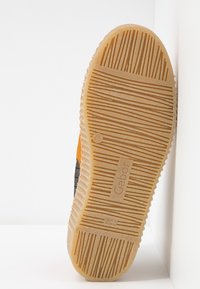 Semelle de basket en caoutchouc avec une semelle à motifs. Les couleurs incluent beige, orange et noir. Surface texturée avec un logo embossé sur le côté.