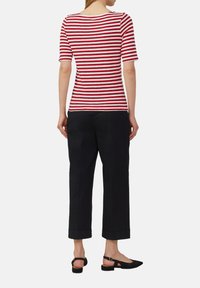 Haut à manches courtes rayé rouge et blanc avec un col arrondi, associé à un pantalon noir court et des sandales noires.