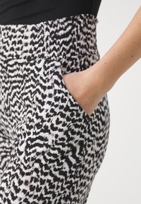 Pantalons à motifs noir et blanc avec une taille élastique et des poches latérales, fabriqués dans un tissu fluide et texturé.